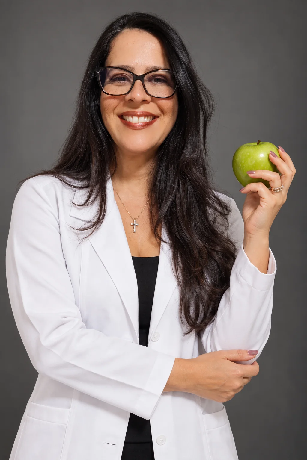 Retrato de Jamile Baptista de jaleco branco, sorrindo e segurando uma maçã verde